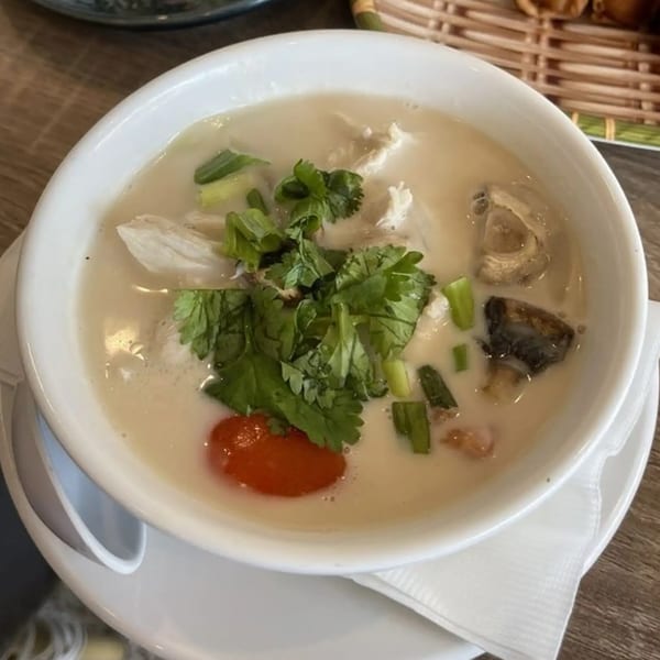 A white bowl of NUA Thai Tom Kha Gai soup with chicken, mushrooms, cilantro, and red chili.