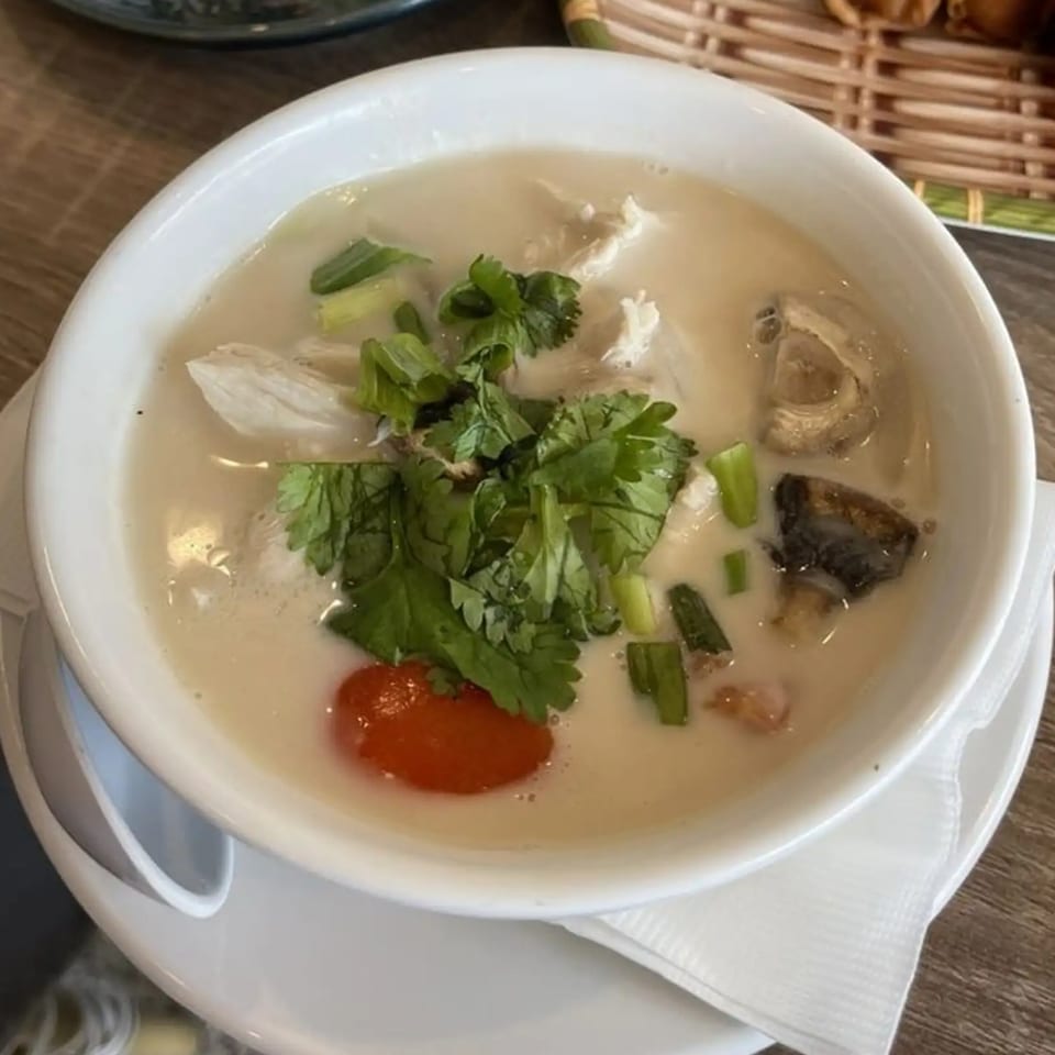 A white bowl of NUA Thai Tom Kha Gai soup with chicken, mushrooms, cilantro, and red chili.