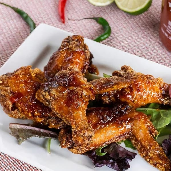 NUA Thai's crispy fried chicken wings glazed with sauce, served on a white plate with greens.