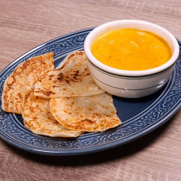 NUA Thai's golden curry in a white bowl with crispy roti bread on a blue plate.