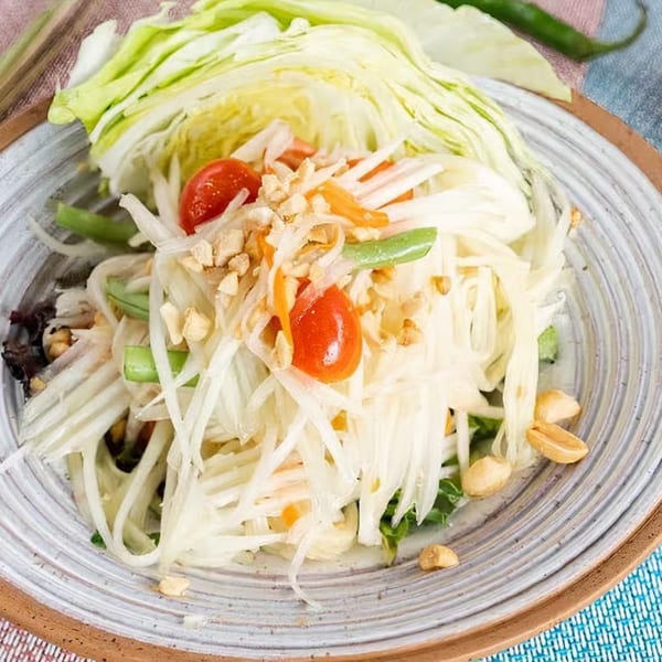 NUA Thai papaya salad with shredded papaya, tomatoes, green beans, and peanuts on a plate.