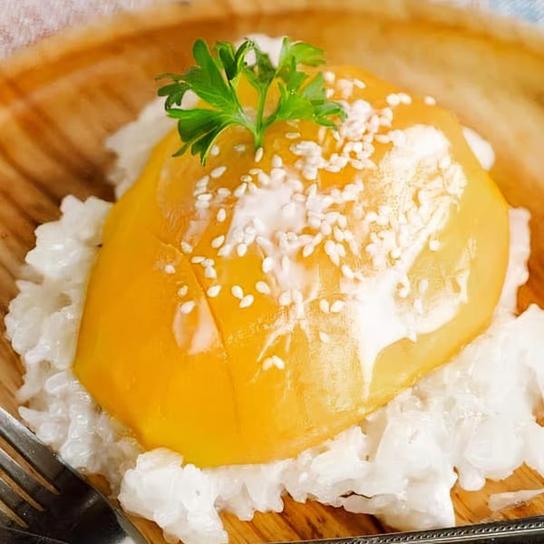 NUA Thai mango sticky rice dessert with coconut cream, sesame seeds, and a parsley garnish.